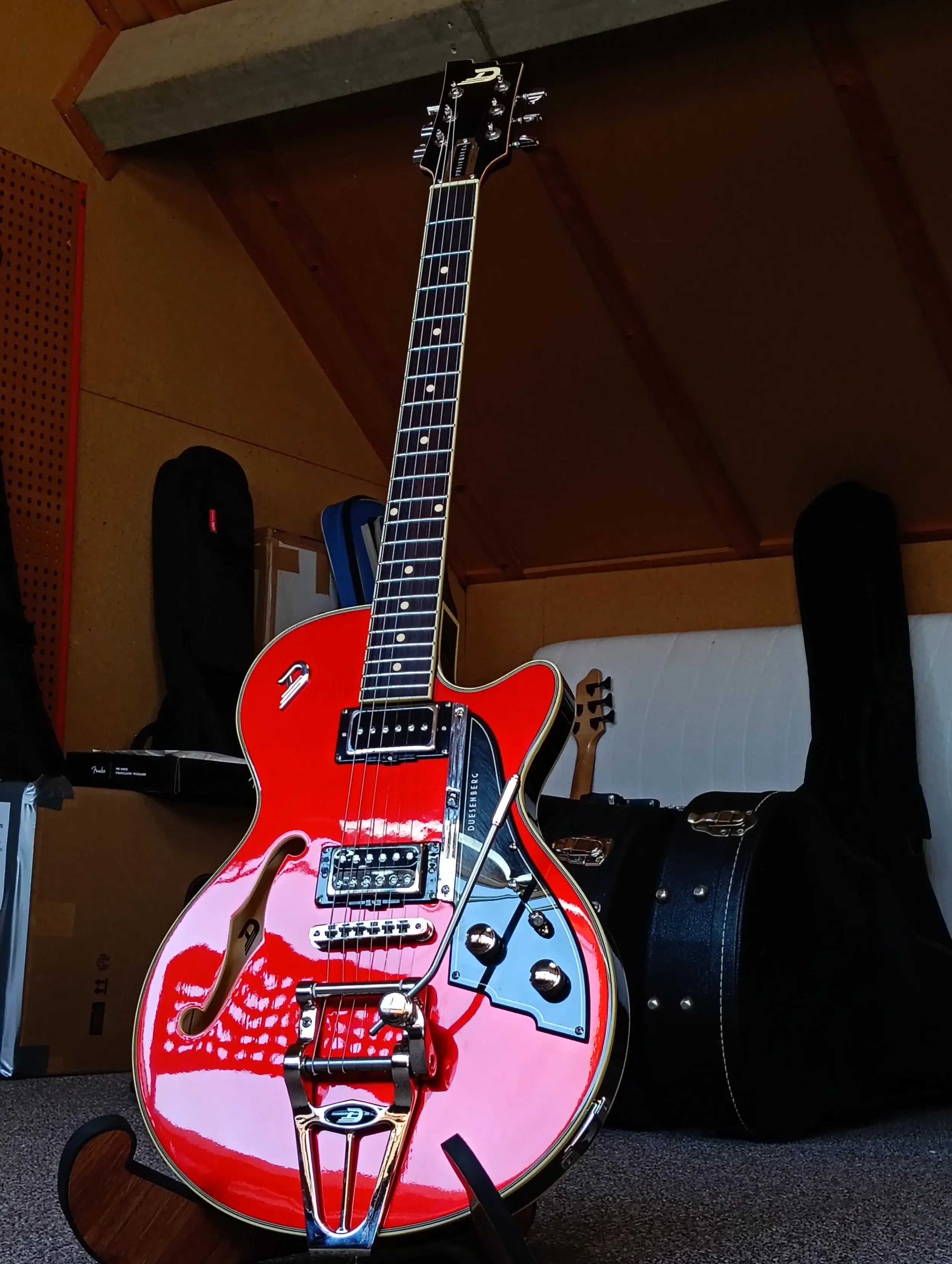 Rode hollowbody-gitaar met vibrato-staartstuk op een standaard in de werkplaats, klaar om opgehaald te worden.