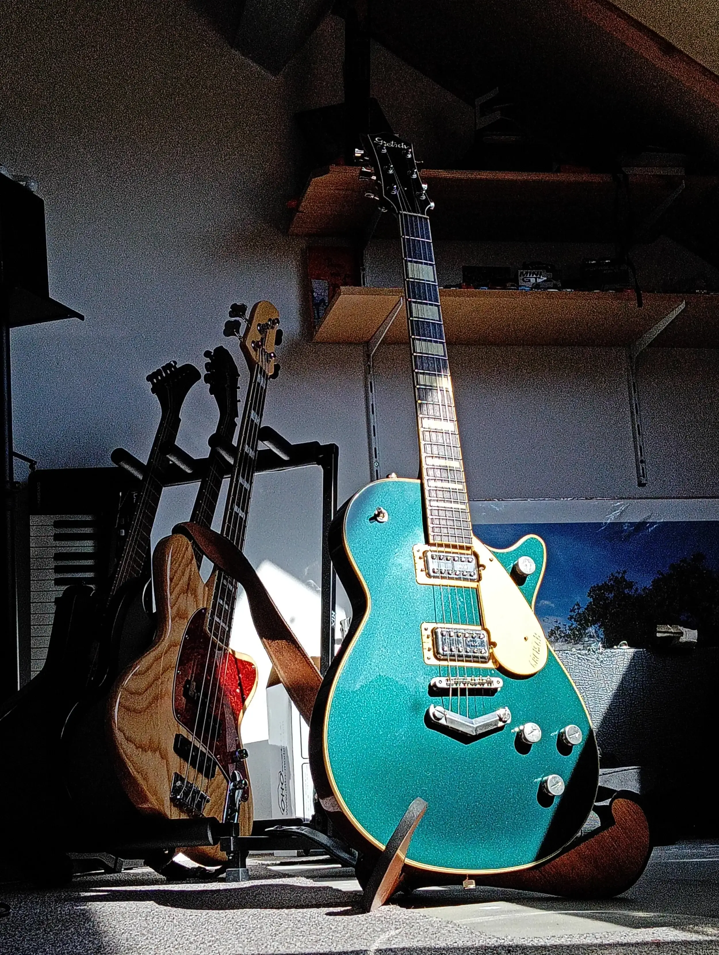 Zeegroene single-cut gitaar met gouden hardware op een standaard, naast een bas met gevlamde top.