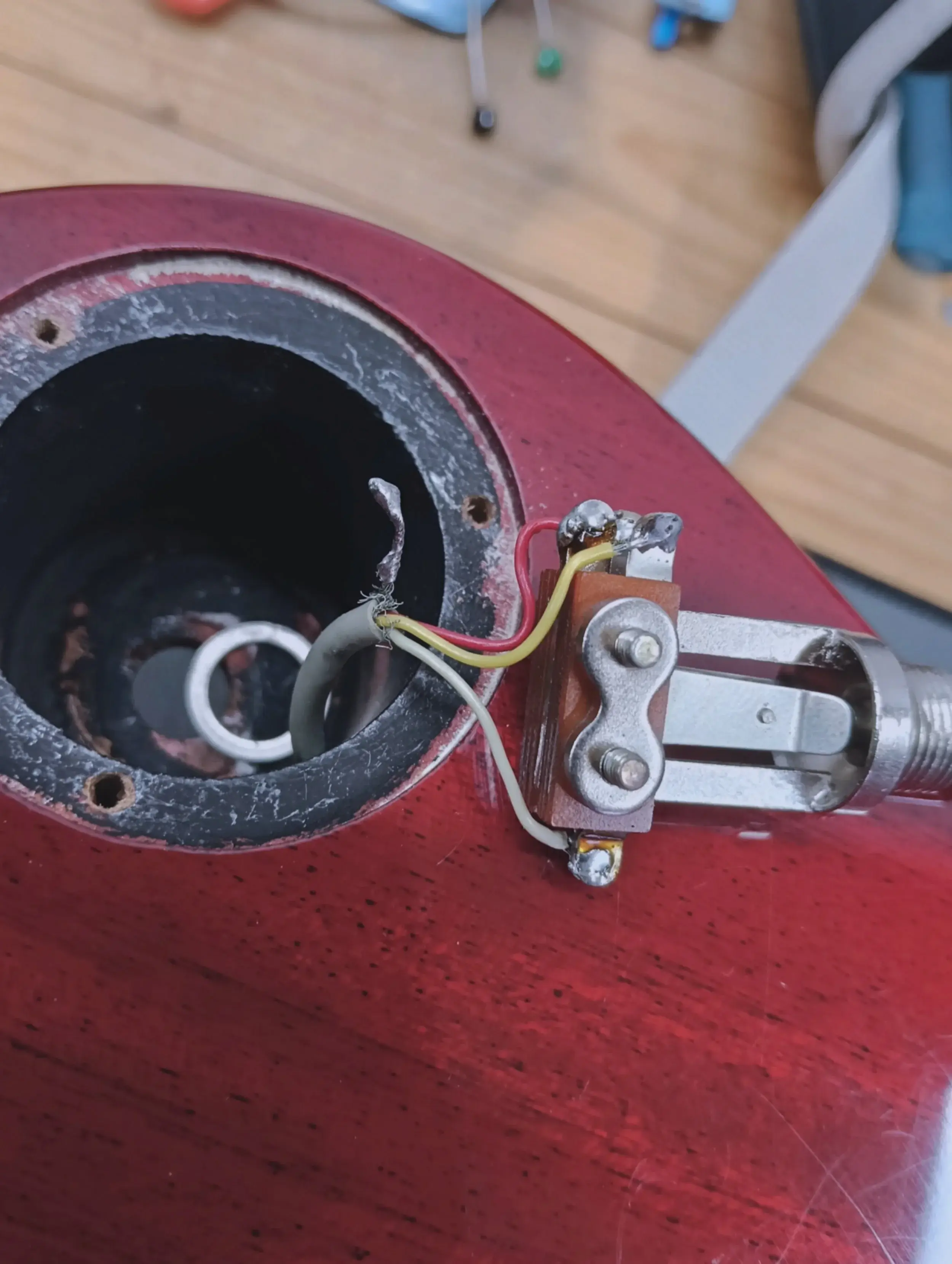 Open elektronicavak van een rode gitaar tijdens het bedraden, met de jackplug en losse draden zichtbaar.